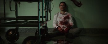 Movie still from “Southbound” (2015), directed by Tyler Gillett – A man sitting on the ground with blood on his face; Medium shot, High angle