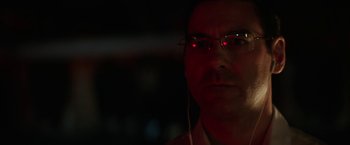 Movie still from “Southbound” (2015), directed by Tyler Gillett – A man wearing glasses and headphones with red lights in the background; Close Up shot, Over the shoulder angle