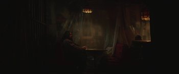 Movie still from “Southbound” (2015), directed by Tyler Gillett – A man sitting at a table in front of a window; Wide shot, Low angle