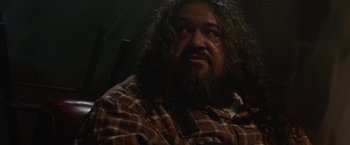 Movie still from “Southbound” (2015), directed by Tyler Gillett – A man with long hair and a beard is sitting; Close Up shot, Over the shoulder angle