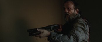 Movie still from “Southbound” (2015), directed by Tyler Gillett – A man holding a gun in a room; Close Up shot, Over the shoulder angle