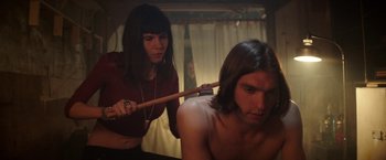 Movie still from “Southbound” (2015), directed by Tyler Gillett – A woman holding a wooden stick over a man's face; Medium shot, Low angle