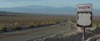 Movie still from “Southbound” (2015), directed by Tyler Gillett – A car driving down a road in the middle of the desert; Extreme Wide shot, High angle