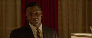 Movie still from “Sparkle” (2012), directed by Salim Akil – A man wearing a suit and tie in front of a red curtain; Close Up shot, Over the shoulder angle