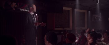 Movie still from “Sparkle” (2012), directed by Salim Akil – A man standing on a microphone in front of a group of people; Medium shot, Over the shoulder angle