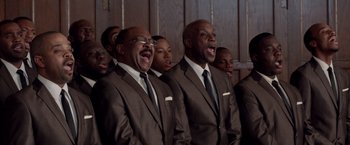 Movie still from “Sparkle” (2012), directed by Salim Akil – A group of men in brown suits singing in front of a wooden wall; Medium shot, High angle