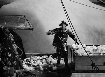Movie still from “Spawn of the North” (1938), directed by Henry Hathaway – A man standing in front of a pile of wool; Wide shot, High angle