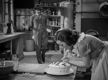 Movie still from “Spawn of the North” (1938), directed by Henry Hathaway – A man and a woman in a kitchen with a cake on the table; Medium shot, High angle