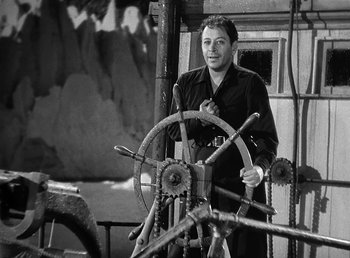 Movie still from “Spawn of the North” (1938), directed by Henry Hathaway – A black and white photo of a man standing next to a steering wheel; Medium shot, High angle