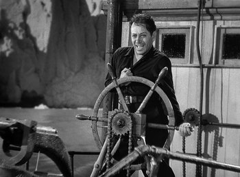 Movie still from “Spawn of the North” (1938), directed by Henry Hathaway – A black and white photo of a man smiling at the camera while sitting at the wheel of a boat; Medium shot, High angle
