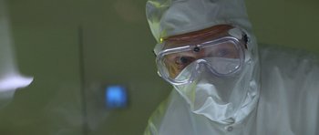 Movie still from “Species” (1995), directed by Roger Donaldson – A person in a lab coat and goggles looking at the camera; Close Up shot, Low angle