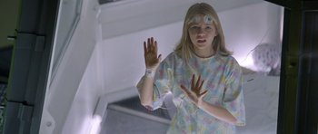 Movie still from “Species” (1995), directed by Roger Donaldson – A young girl in a hospital gown is holding her hands up; Medium shot, High angle
