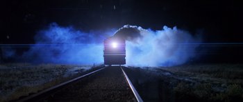 Movie still from “Species” (1995), directed by Roger Donaldson – A train traveling down train tracks at night with smoke billowing out of it; Extreme Wide shot, Low angle