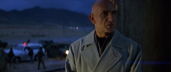 Movie still from “Species” (1995), directed by Roger Donaldson – A bald man wearing a trench coat standing next to a street; Close Up shot, Low angle