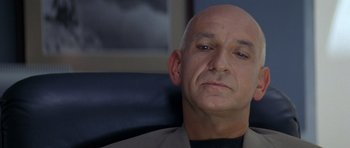 Movie still from “Species” (1995), directed by Roger Donaldson – A bald man sitting in an office chair looking sad; Close Up shot, Low angle