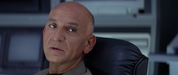 Movie still from “Species” (1995), directed by Roger Donaldson – A man sitting in an office chair with his head tilted to the side; Close Up shot, High angle