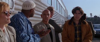 Movie still from “Species” (1995), directed by Roger Donaldson – A group of men standing next to each other near a train; Medium shot, Over the shoulder angle
