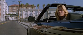 Movie still from “Species” (1995), directed by Roger Donaldson – A woman driving a car down a street with palm trees in the background; Medium shot, Low angle