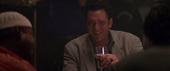 Movie still from “Species” (1995), directed by Roger Donaldson – A man holding a glass of beer while sitting down; Close Up shot, Over the shoulder angle