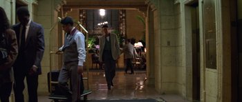 Movie still from “Species” (1995), directed by Roger Donaldson – A man in a suit walking in a hotel lobby; Wide shot, Over the shoulder angle