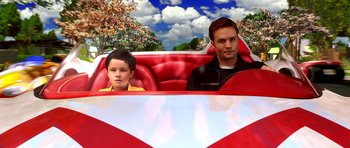 Movie still from “Speed Racer” (2008), directed by Lilly Wachowski – A man and a boy sitting in the back seat of a red car; Medium shot, Low angle