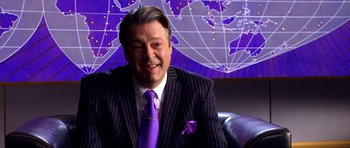 Movie still from “Speed Racer” (2008), directed by Lilly Wachowski – A man in a suit and tie sitting in front of a map of the world; Medium shot, High angle