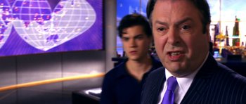 Movie still from “Speed Racer” (2008), directed by Lilly Wachowski – A man in a suit and tie standing next to another man in a suit and tie; Close Up shot, Over the shoulder angle