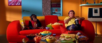 Movie still from “Speed Racer” (2008), directed by Lilly Wachowski – Two people sitting on a red couch eating food; Wide shot, High angle