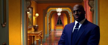 Movie still from “Speed Racer” (2008), directed by Lilly Wachowski – A man wearing a suit and tie in a room with yellow walls; Medium shot, Over the shoulder angle