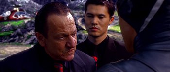 Movie still from “Speed Racer” (2008), directed by Lilly Wachowski – A man in a suit and tie standing next to another man in a suit and tie; Close Up shot, Over the shoulder angle