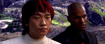 Movie still from “Speed Racer” (2008), directed by Lilly Wachowski – A man with red hair and a white shirt is standing next to another man; Close Up shot, Over the shoulder angle