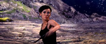 Movie still from “Speed Racer” (2008), directed by Lilly Wachowski – A woman in a black tank top holding a stick in her hand; Medium shot, Over the shoulder angle