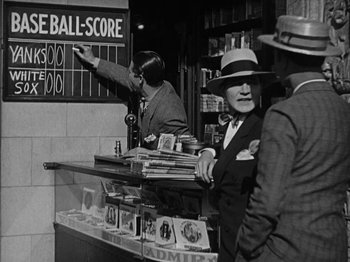 Movie still from “Speedy” (1928), directed by Ted Wilde – An old photo of a man in a suit and a hat standing in front of a store; Medium shot, Low angle