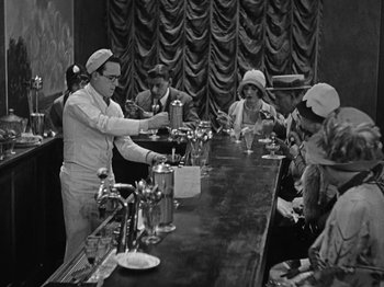 Movie still from “Speedy” (1928), directed by Ted Wilde – A group of people sitting around a bar; Wide shot, High angle