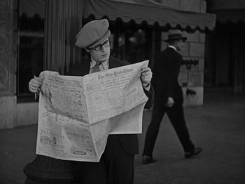 Movie still from “Speedy” (1928), directed by Ted Wilde – A man wearing a hat and reading a newspaper; Medium shot, High angle