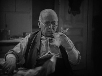 Movie still from “Speedy” (1928), directed by Ted Wilde – An old man sitting at a table smoking a cigarette; Medium shot, High angle