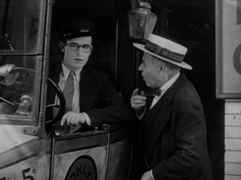 Movie still from “Speedy” (1928), directed by Ted Wilde – A man in a suit and a hat is talking to another man in a hat; Medium shot, Over the shoulder angle