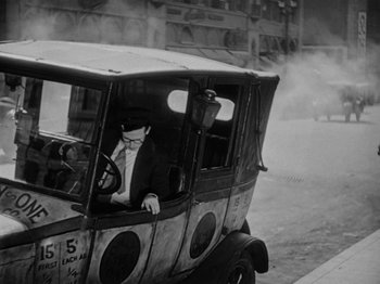 Movie still from “Speedy” (1928), directed by Ted Wilde – An old fashioned car driving down the street; Wide shot, High angle