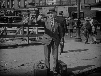 Movie still from “Speedy” (1928), directed by Ted Wilde – An old black and white photo of a man in a suit and hat; Wide shot, High angle