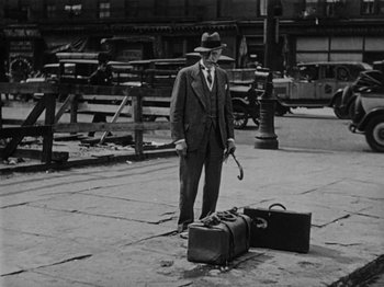 Movie still from “Speedy” (1928), directed by Ted Wilde – An old photo of a man standing next to luggage; Wide shot, Low angle