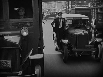 Movie still from “Speedy” (1928), directed by Ted Wilde – An old photo of a man riding a scooter in front of an old truck; Wide shot, Low angle