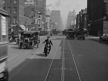 Movie still from “Speedy” (1928), directed by Ted Wilde – An old photo of a man riding a motorcycle down the street; Extreme Wide shot, High angle