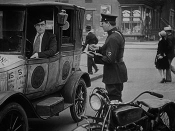 Movie still from “Speedy” (1928), directed by Ted Wilde – An old photo of two men in a car and a motorcycle; Wide shot, Low angle