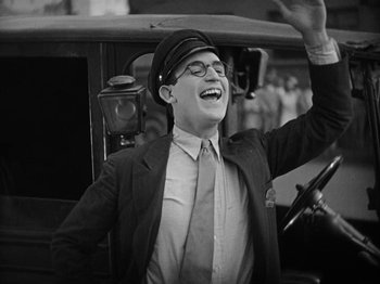 Movie still from “Speedy” (1928), directed by Ted Wilde – A man wearing a hat and glasses is smiling; Medium shot, Low angle