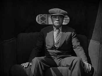 Movie still from “Speedy” (1928), directed by Ted Wilde – A man sitting on a couch wearing a suit and a hat; Medium shot, Low angle
