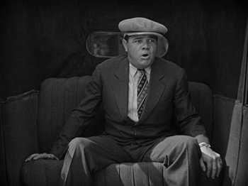 Movie still from “Speedy” (1928), directed by Ted Wilde – A man sitting on top of a couch wearing a suit and hat; Medium shot, High angle
