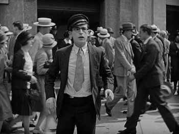Movie still from “Speedy” (1928), directed by Ted Wilde – A man wearing a hat and a tie standing in front of a group of people; Medium shot, Low angle