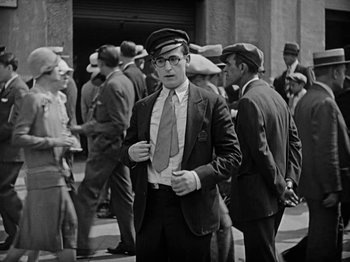 Movie still from “Speedy” (1928), directed by Ted Wilde – A man wearing a hat and a tie standing next to a crowd; Medium shot, High angle