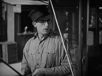 Movie still from “Speedy” (1928), directed by Ted Wilde – A man wearing glasses and a hat standing in front of a window; Close Up shot, Low angle