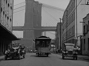 Movie still from “Speedy” (1928), directed by Ted Wilde – An old picture of a street with cars and a bridge in the background; Extreme Wide shot, Low angle